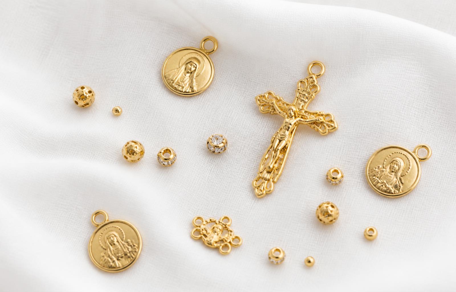 Componentes dourados para terços: crucifixo, medalhas e contas sobre tecido de linho branco